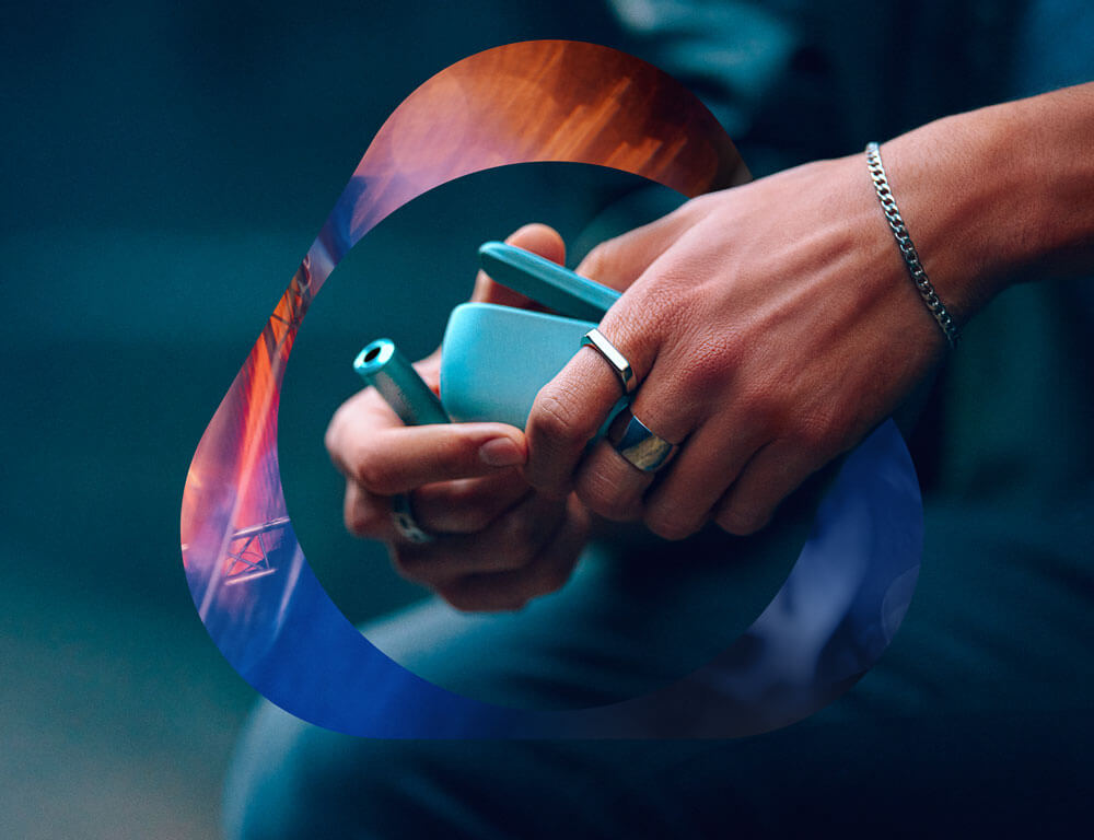 A man's hand holding an IQOS ILUMA i Breeze Blue device