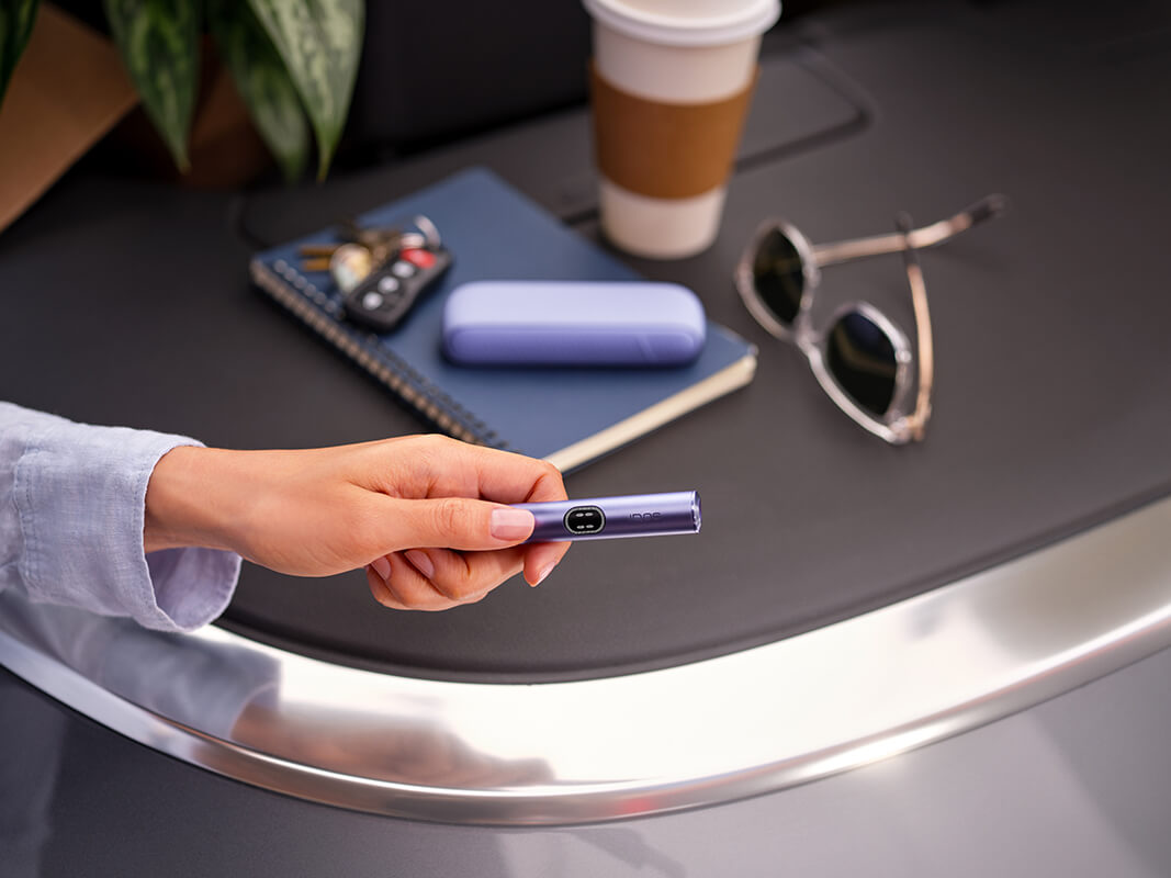 A man holding his iqos device next to a laptop