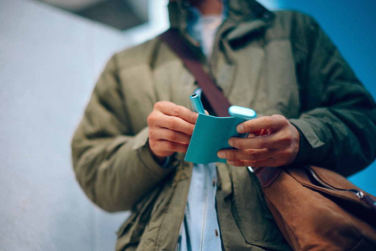 En Jade Green IQOS ILUMA PRIME-hållare och fickladdare i en persons händer.