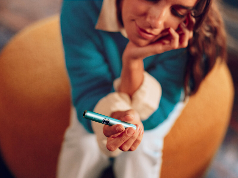 A smiling woman with an IQOS ILUMA device