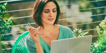 A woman holding an IQOS device looking at a laptop.