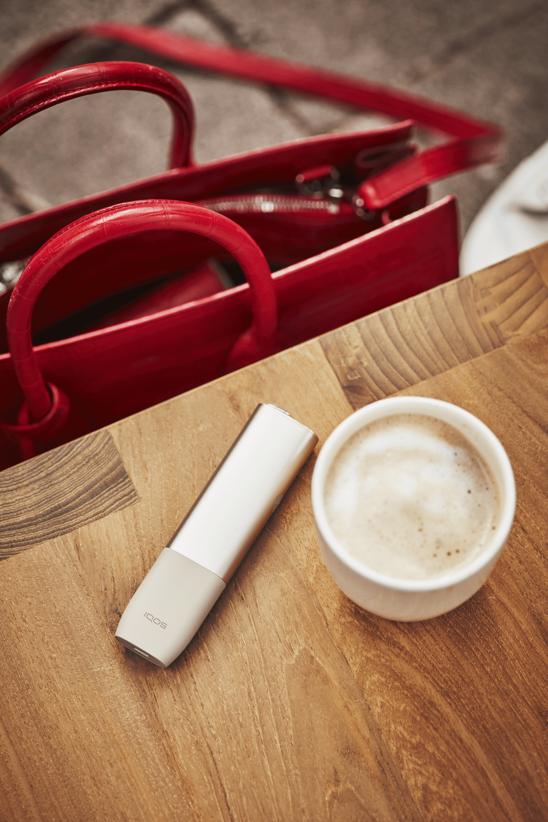 A rose gold IQOS next to a coffee