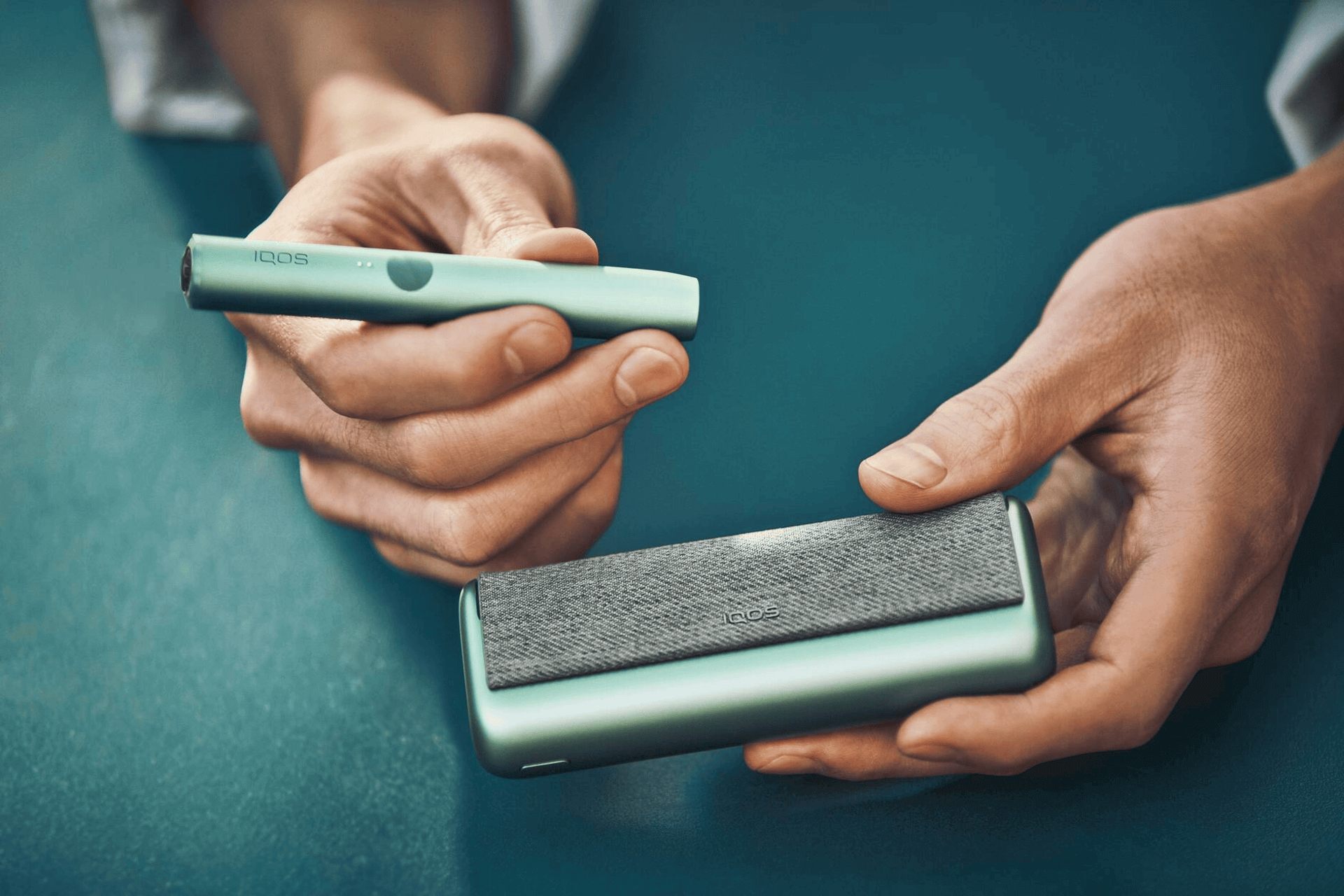 A Jade Green IQOS ILUMA PRIME Holder and Pocket Charger in a person's hands.