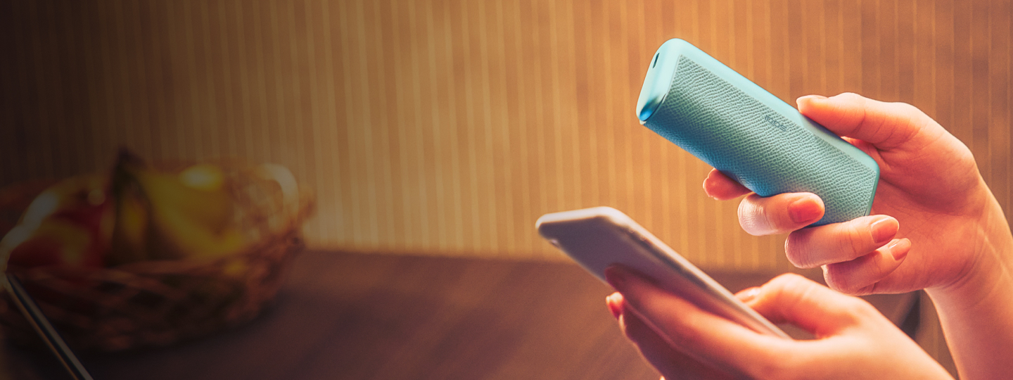 Händer som håller i en blå IQOS ILUMA-enhet och en telefon