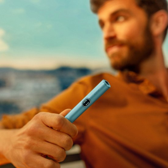 Black IQOS ILUMA i PRIME device; yellow paper on a table in the background
