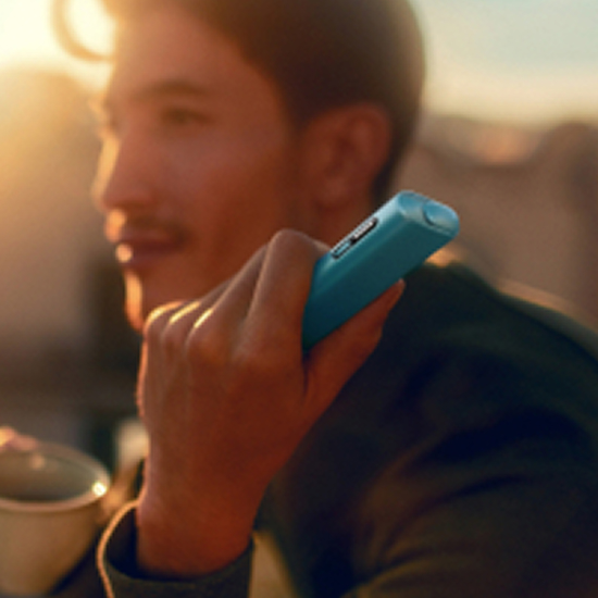 Man som håller i en IQOS ILUMA i ONE-enhet, bakgrund med solnedgång