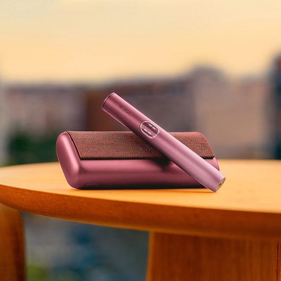 Garnet Red IQOS ILUMA i PRIME-enhet ovanför dess laddare på ett bord