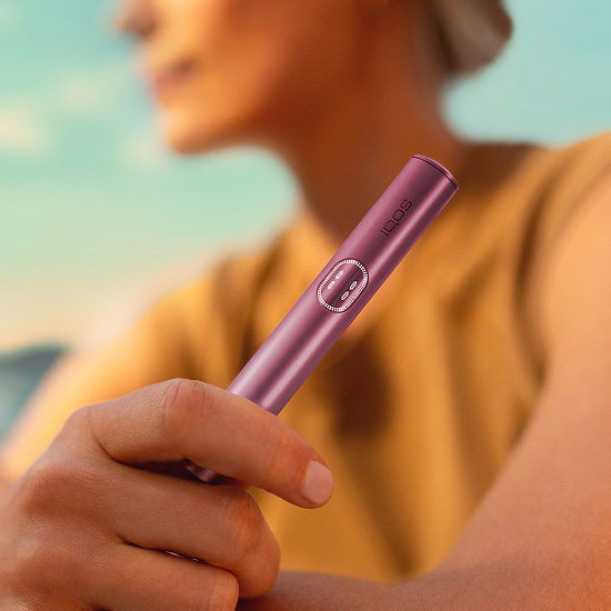 Kvinna som håller i en Garnet Red IQOS ILUMA i PRIME-enhet
