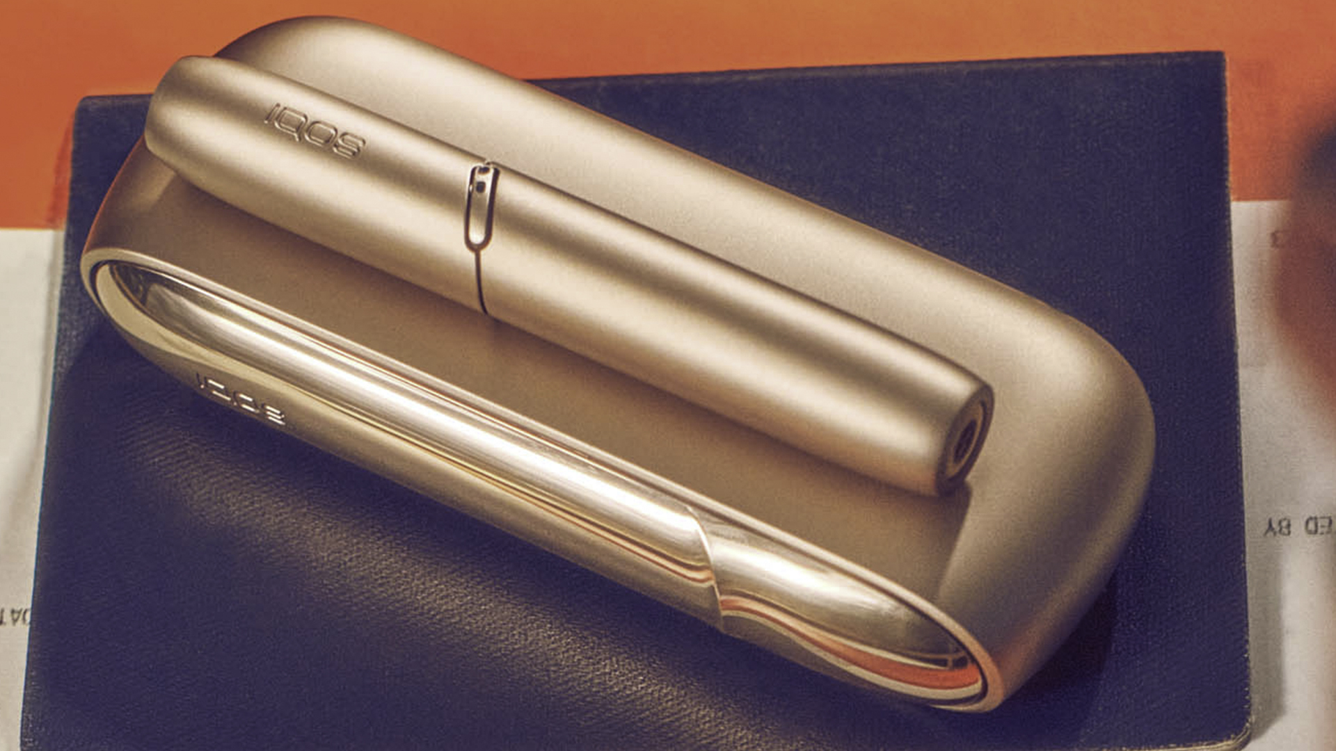 A gold IQOS DUO device on an orange copybook