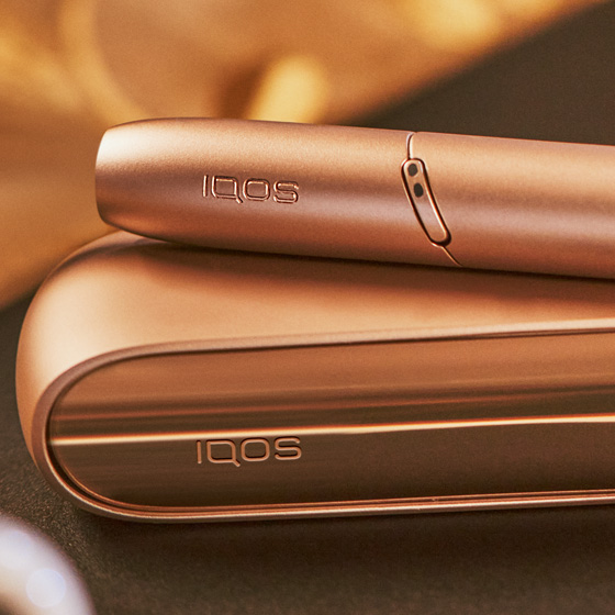 Brilliant gold IQOS 3 DUO holder and charger next to binoculars