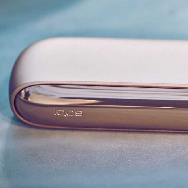 Man with phone in one hand, IQOS device in the other who is trying to follow IQOS guidelines
