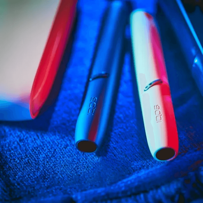 Brilliant gold IQOS 3 DUO with HEETS stick and charger next to binoculars on a blue blanket
