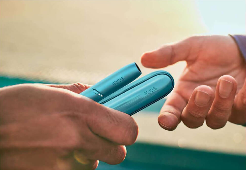 hand giving an iqos device to another hand
